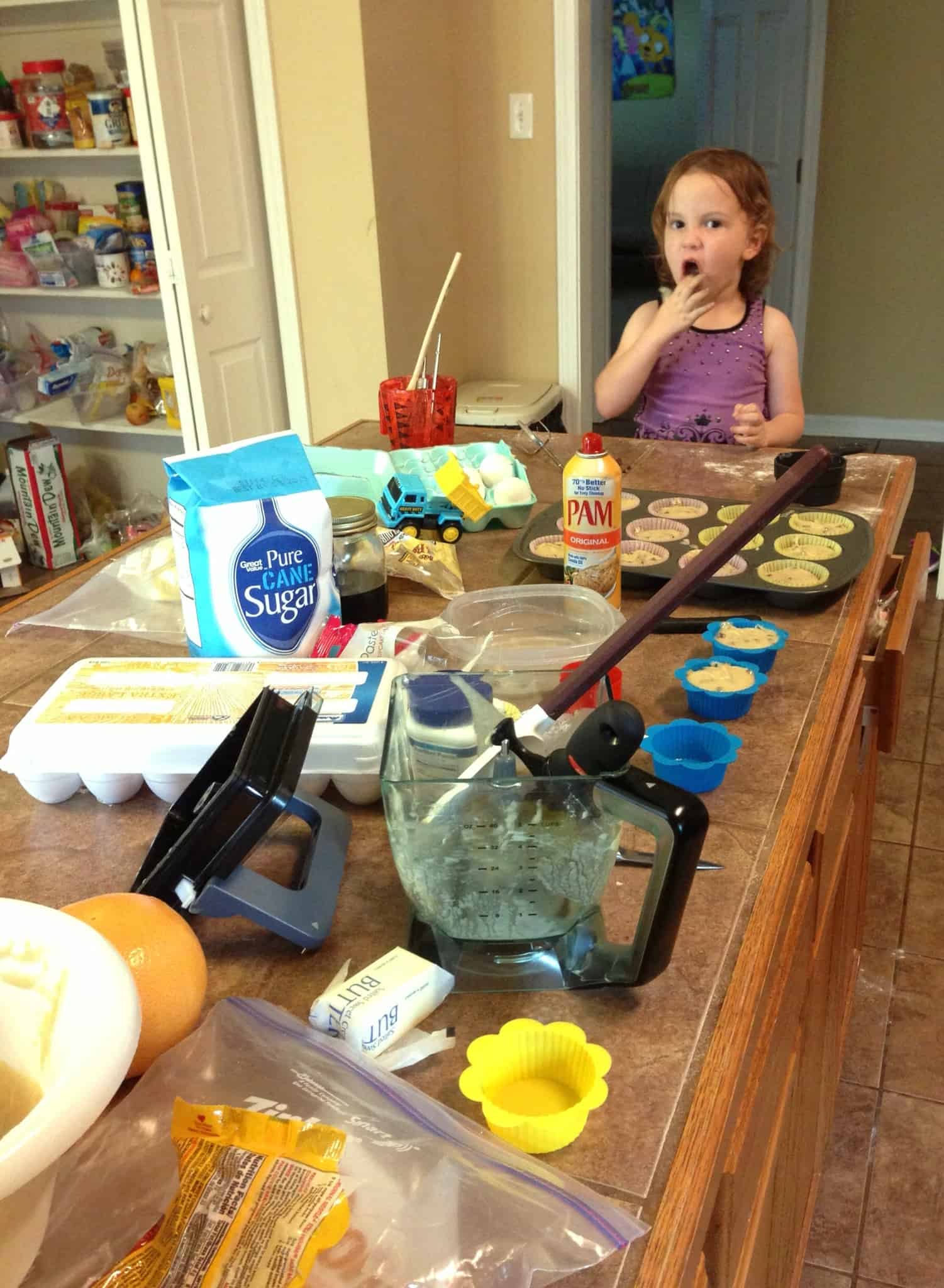 Little girl sitting at a messy counter, baking.