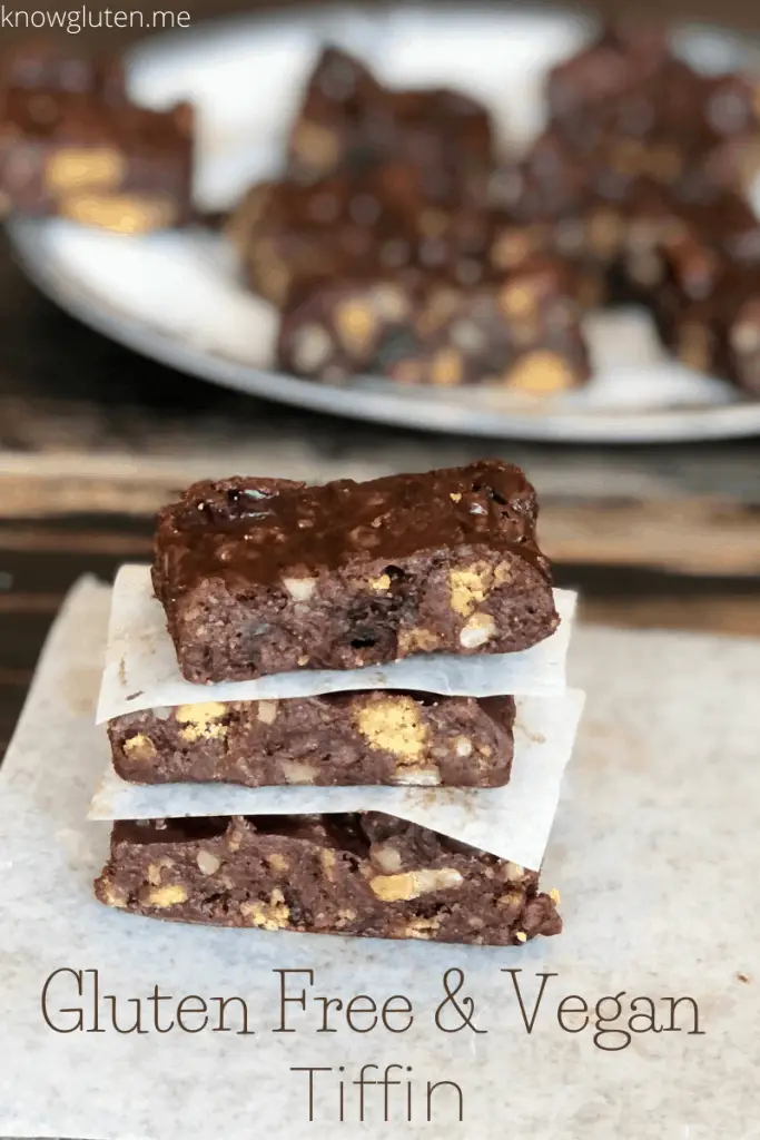 3 pieces of gluten free & vegan tiffin stacked on a piece of parchment paper with a plate full of tiffin behind it.