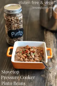 a bowl of pinto beans beside a jar of dried pinto beans with a pressure cooker in the background