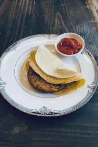 a gluten free, vegan breakfast sandwich on a china plate with a side dish of ketchup