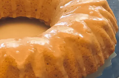 A closeup of a gluten free vanilla bundt cake with a glaze on a glass serving tray.